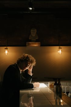 一个男人穿着西装，独自坐在灯光昏暗的酒吧柜台前，显得深思熟虑，散发着阴沉的心情
