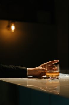 酒吧柜台的光线昏暗，一只手拿着一杯威士忌