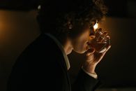 一位时尚的年轻人穿着西装，在灯光昏暗的酒吧里喝着饮料