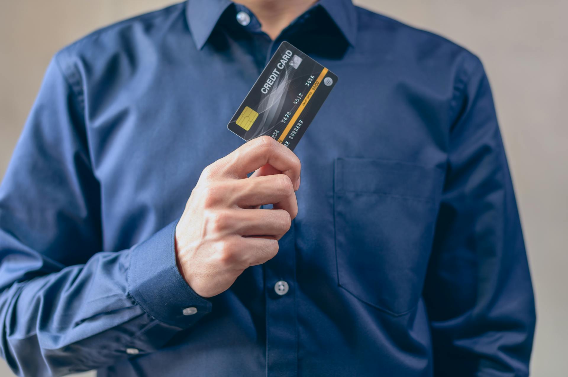 Close-up of a man in a blue shirt holding a credit card, symbolizing finance and security.