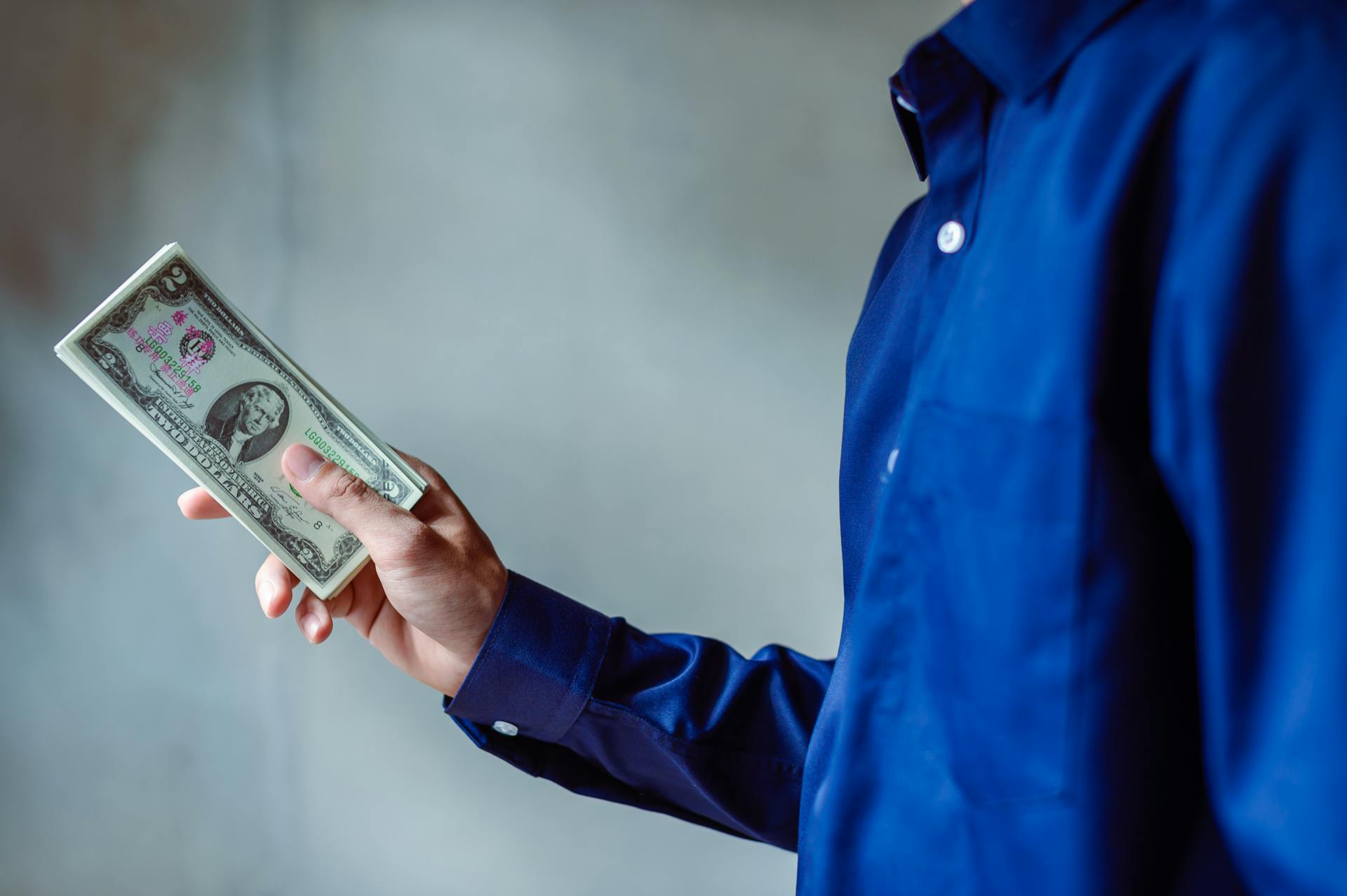 A person in a blue shirt holding a stack of US dollar bills, symbolizing wealth and finance.