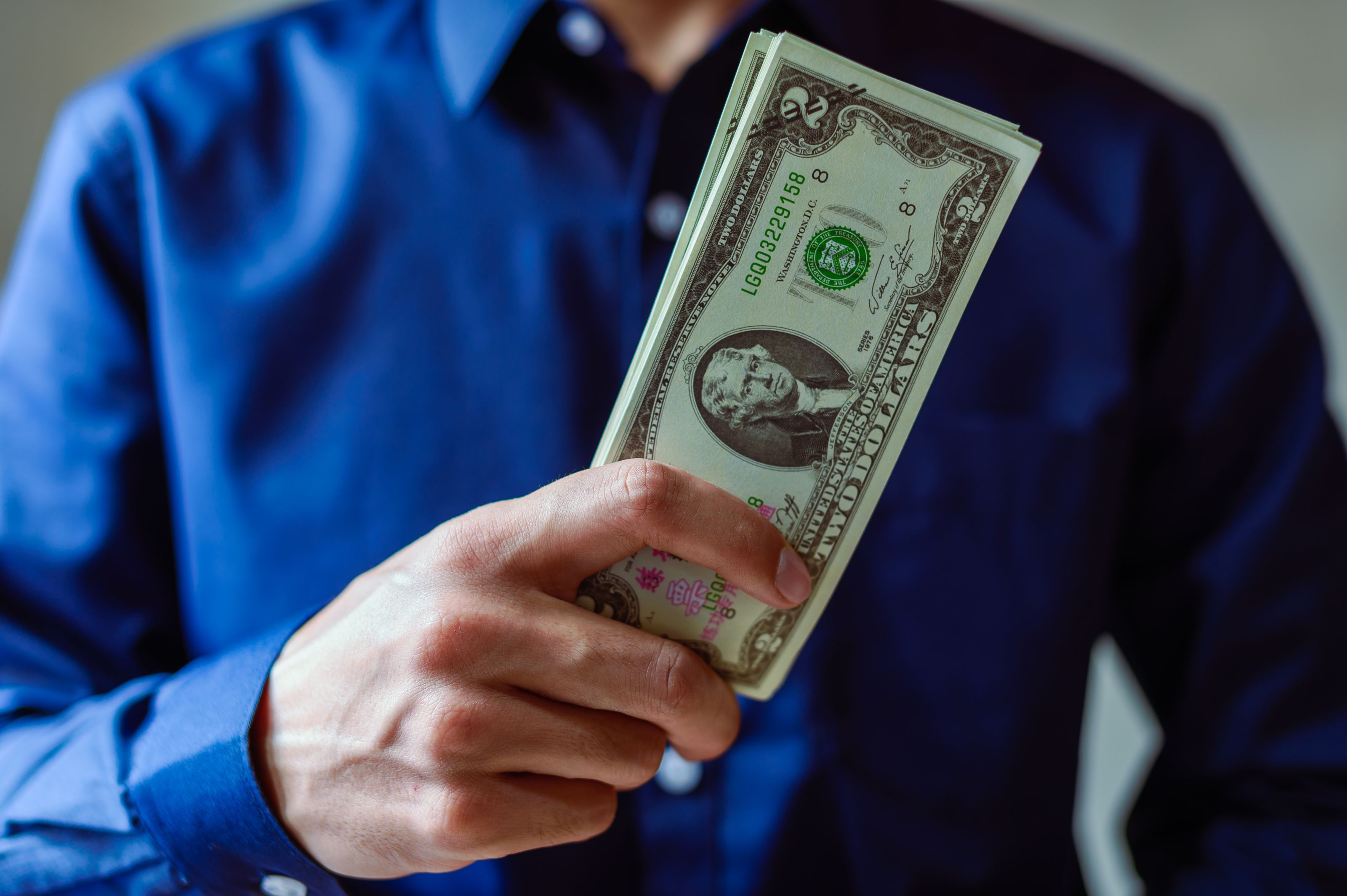 Close-up of a person holding two dollar bills, representing wealth and finance.
