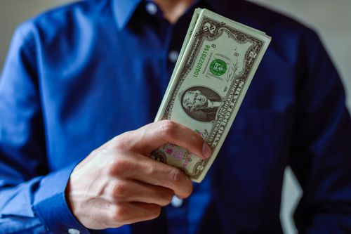 Free Close-up of a person holding two dollar bills, representing wealth and finance. Stock Photo