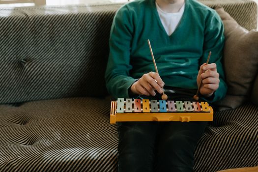 A child in a green sweater plays a colorful xylophone while sitting on a sofa indoors.