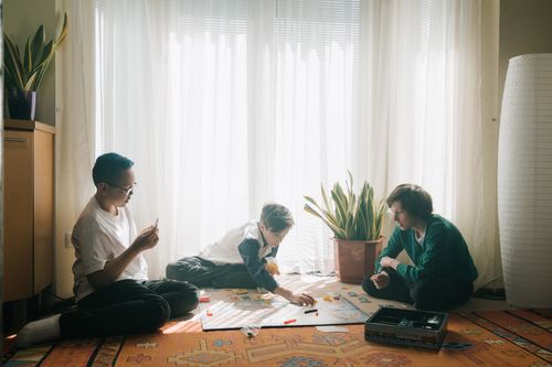 Free Three teenagers engaged in a strategic board game in a sunlit living room, fostering teamwork and fun. Stock Photo