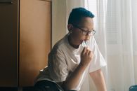 一个戴着眼镜、蓝头发的小男孩在室内若有所思地拿着一张卡片，展现了他的专注