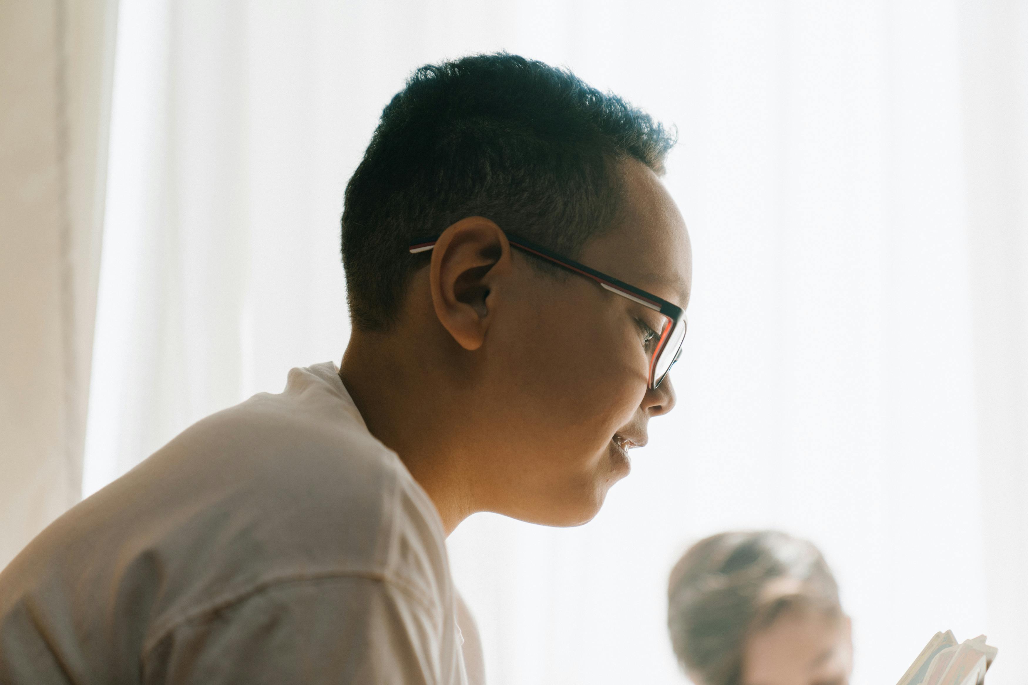A young student with glasses engaged in reading indoors, highlighting focus and learning.