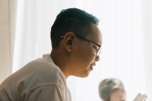 Free A young student with glasses engaged in reading indoors, highlighting focus and learning. Stock Photo