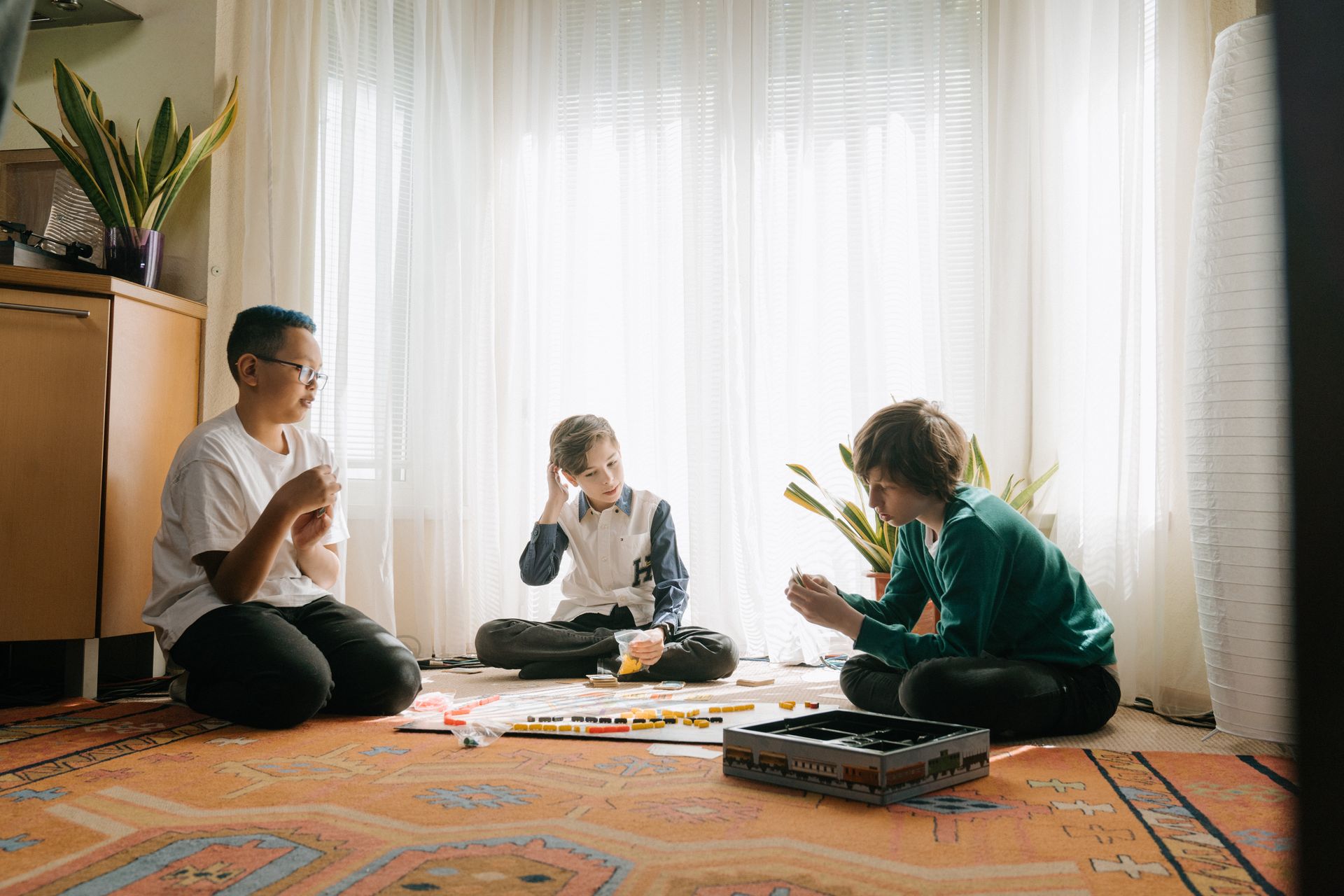 Three children playing a tabletop game indoors on a sunny day. Perfect for themes of friendship and leisure.