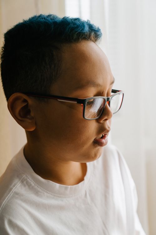 Free Side profile portrait of a young boy with blue hair wearing glasses. Natural light indoors. Stock Photo