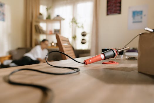 Close-up of a soldering iron on a wooden table at home with a blurred background for tech projects.