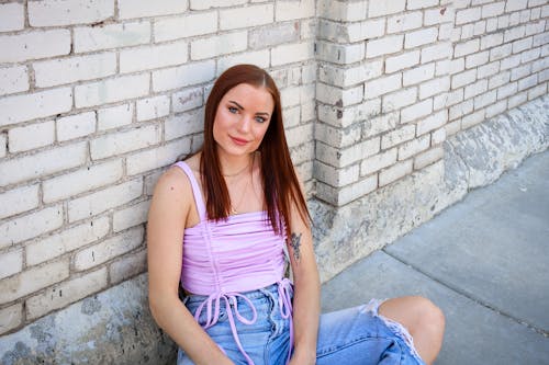 Free Woman Leaning on a Brickwall and Sitting on Concrete Floor Stock Photo