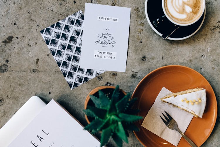 Cup Of Coffee Beside A Card And Slice Of Pie On Brown Plate Beside A Pot Plant