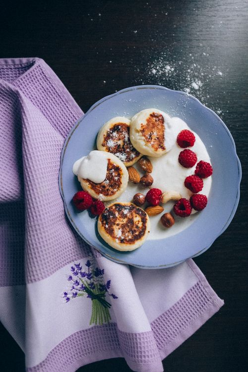Free Mouthwatering syrniki with raspberries, almonds, and cream on a lavender cloth. Stock Photo