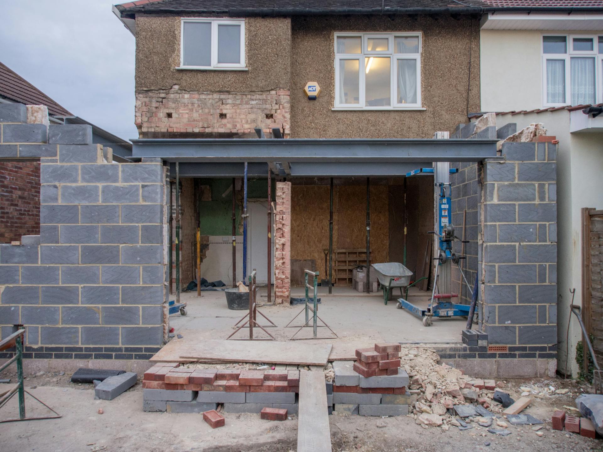 Brick house under renovation with an extension in progress. Visible construction site materials and structure.