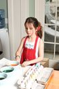 Girl in red apron painting eggs for Easter