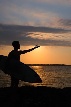 A surfer holds a crystal ball as the sun sets over the ocean, creating a stunning silhouette.
