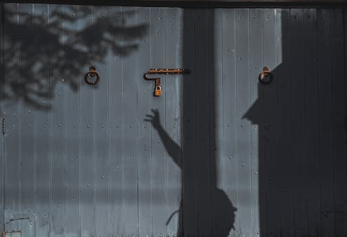 Shadow Reaching to the Padlock on the Wooden Gate