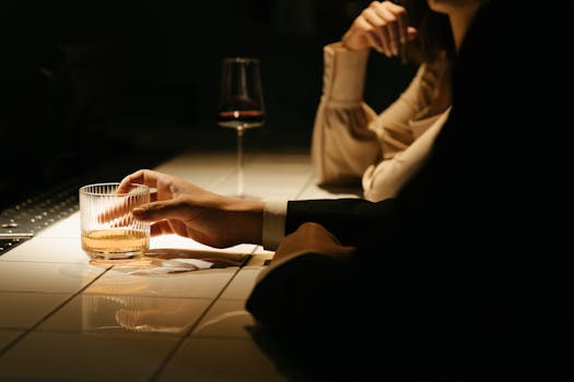 An intimate bar setting with hands holding whiskey and wine, creating a moody atmosphere.