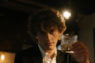 昏暗的酒吧里，一个卷发的男人拿着一杯威士忌