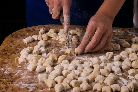 Close-up of hands slicing homemade gnocchi dough on a floured wooden board.