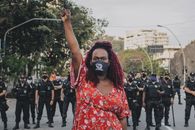 Woman in Floral Dress With Arm Raised Standing In Front of a Group of Policemen