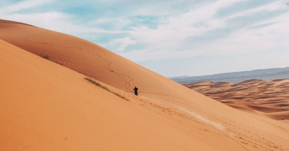 Lone traveler walking across vast Merzouga sand dunes in the Sahara Desert, Morocco — a peaceful moment during the 7 days from Marrakech tour