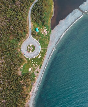 Stunning aerial view of a circular parking area next to a serene ocean shoreline with lush greenery and clear waters.