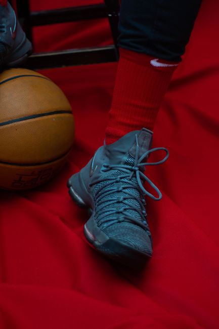 Crop anonymous sportsman in trendy runners and red socks sitting on stool with foot on basketball ball