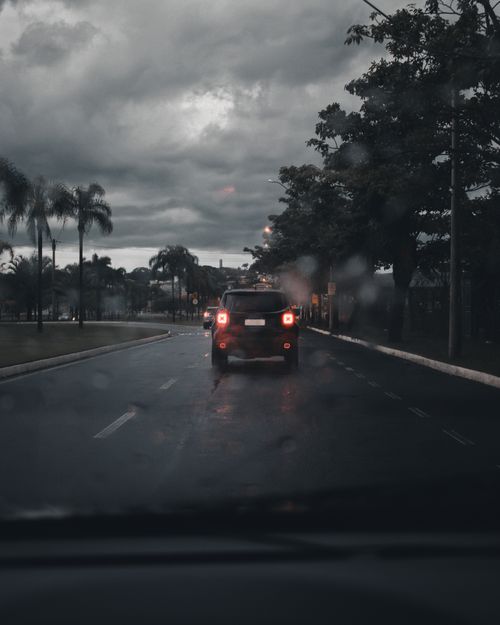 Free A somber urban scene of cars on a rainy road beneath a cloudy sky, capturing the essence of urban transportation. Stock Photo