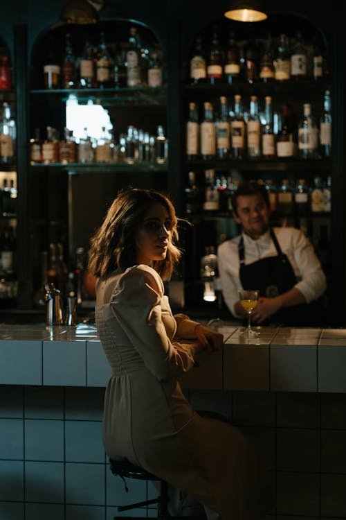 Woman in Gray Long Sleeve Dress Standing in Front of Bar Counter