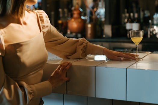 A woman in an elegant dress leans on a bar counter holding a cocktail.
