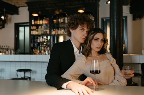 бесплатная Мужчина в черном пиджаке держит прозрачный стакан рядом с женщиной в коричневом пальто Стоковое фото