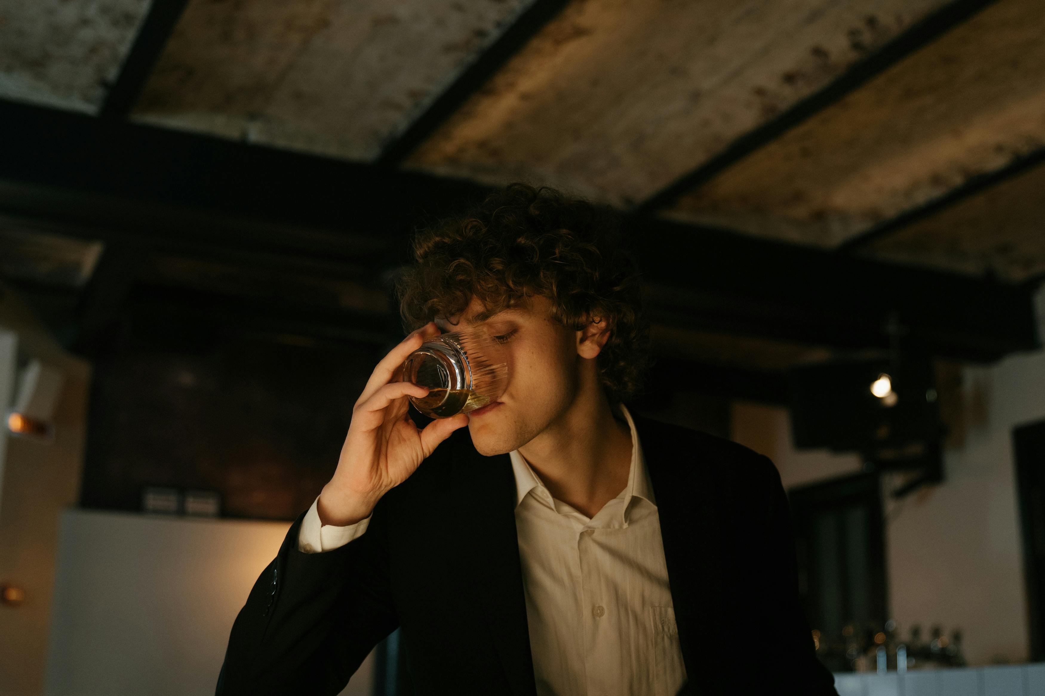 一位穿着黑色西装的时尚男士，在优雅的餐厅里享用着饮品