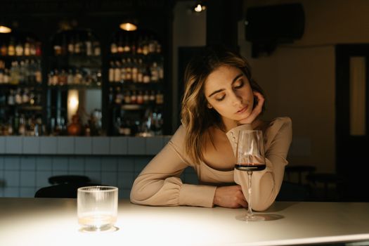 昏暗的灯光下，女人坐在酒吧里，优雅地端着酒杯，气氛十分诱人