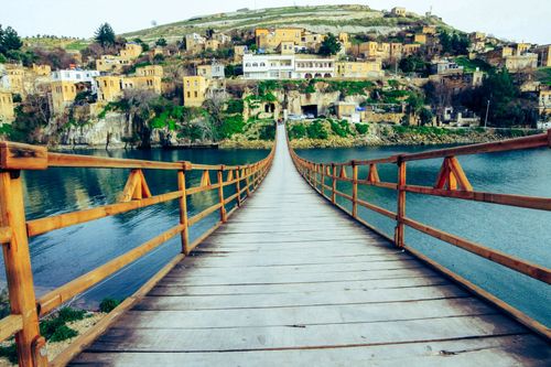 Free Footbridge with wooden railing leading to embankment with houses located on hill in summer time in countryside in daylight outside Stock Photo