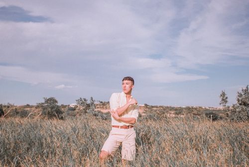 Free A man stands pensively in a grassy field under a clear sky, conveying a thoughtful mood. Stock Photo