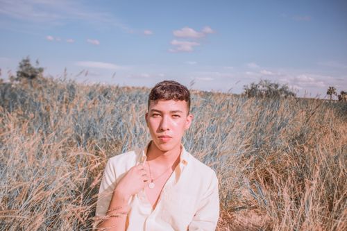 Free A man standing pensively in a sunlit grass field wearing a white dress shirt outdoors. Stock Photo