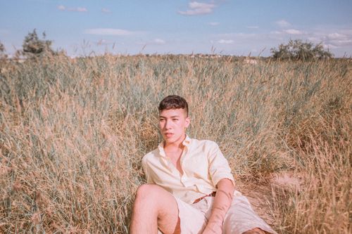 Free A man in a pastel shirt contemplating while lying in a sunny wild grass field. Stock Photo