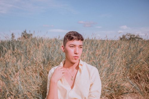 Free A young man poses thoughtfully in a serene, grassy field under a clear blue sky. Stock Photo