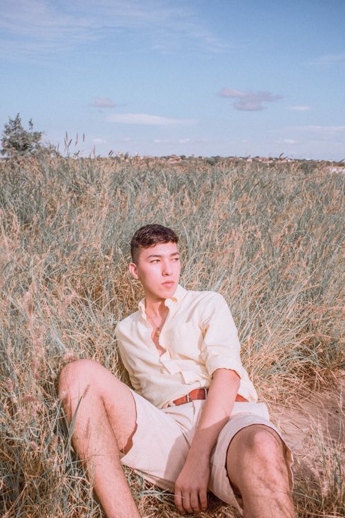 Free Man in a yellow shirt sitting thoughtfully in a grassy field on a sunny day. Stock Photo