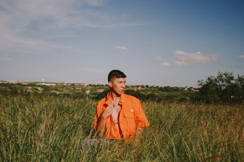 Man in Orange Button Up Shirt Standing on Green Grass Field