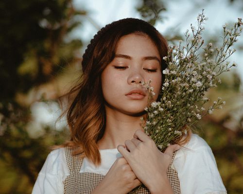 Free Charming brunette with curly hair and closed eyes in casual clothes holding bouquet of fresh lavenders standing in green field Stock Photo