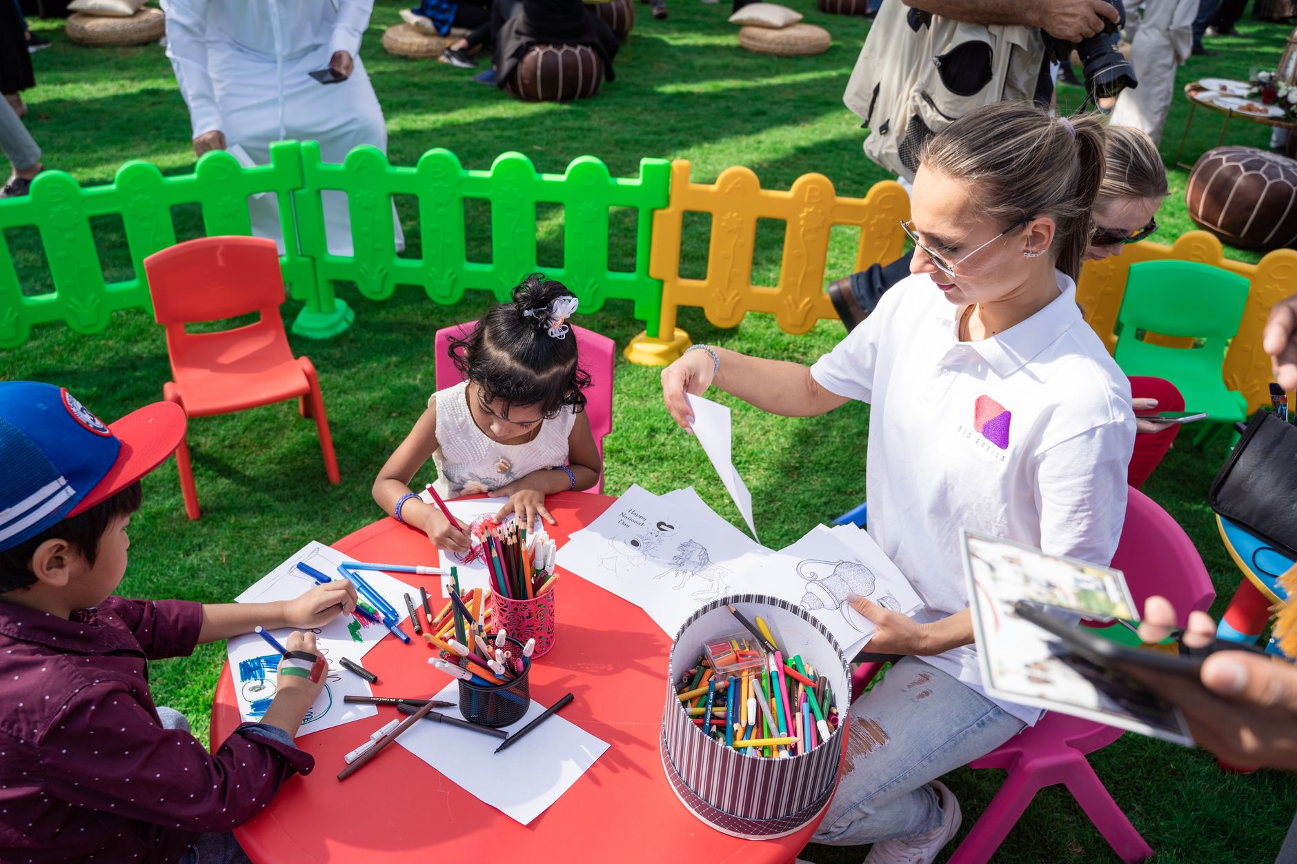 Nile University event planner — Children enjoying drawing and coloring activities outdoors in Dubai with a woman as a guide.