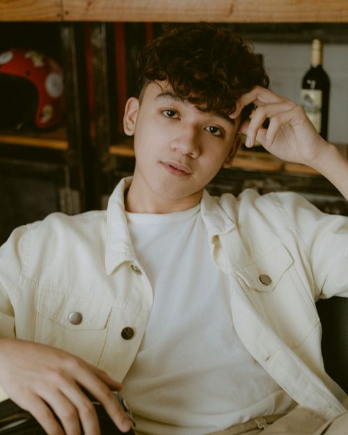 Free Young curly haired male in white shirt posing with hand on head and looking at camera Stock Photo