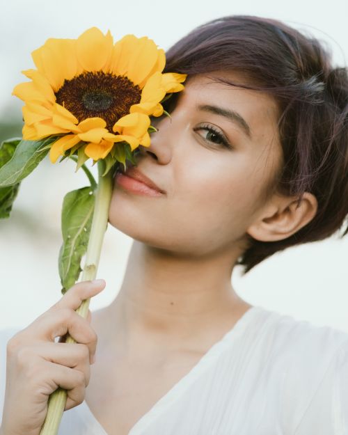 Free Charming woman with short brown hair and light makeup holding fresh sunflower and looking at camera Stock Photo
