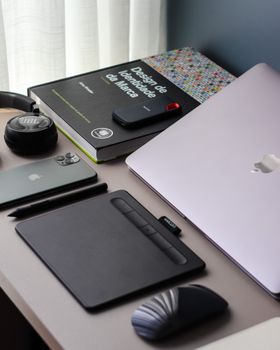 A neatly arranged desk setup featuring a laptop, smartphone, headphones, and drawing tablet.