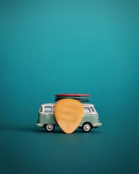 Close-up of a miniature toy van with stacked guitar picks on top, featuring a vibrant teal background.