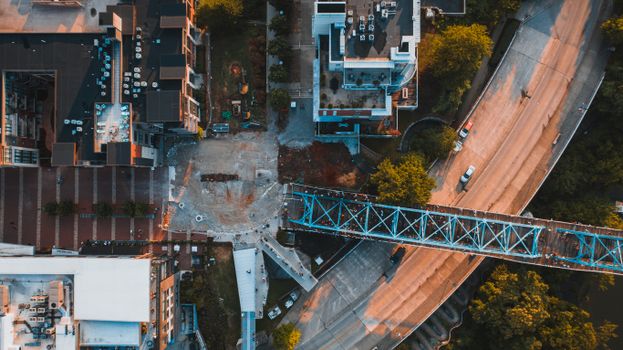 Top view of aged bridge above road with driving vehicles near trees and house roofs