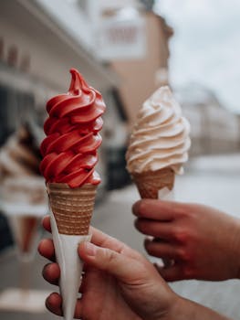A detailed view of hands holding colorful ice cream cones in an outdoor setting.